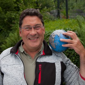 Portraitaufnahme Detlev Fiedrich in einem Garten mit einer kleinen Weltkugel auf der Schulter