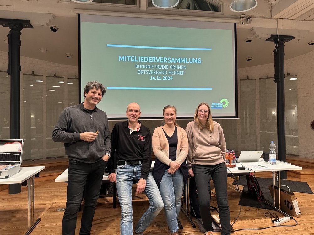 4 Personen vor einem Tisch und im Hintergrund eine Leinwand mit dem Text "Mitgliederversammlung BÜNDNIS90/DIE GRÜNEN, Ortsverband Hennef, 14.11.2024"