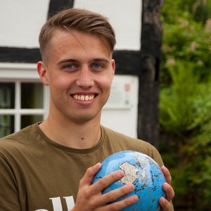 Portraiaufnahme Johannes Noppeney vor einem Gebäude mit einer kleinen Weltkugel in beiden Händen