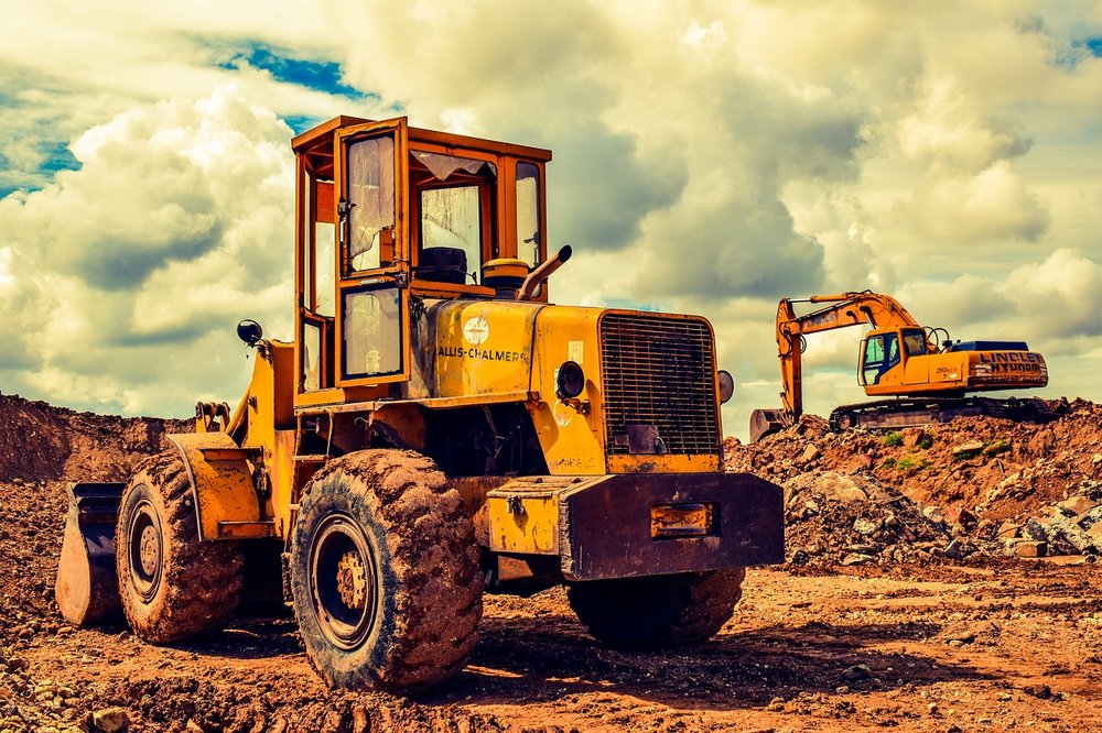 Im Vordergrund planiert ein Bulldozer Fläche mit roter Erde und ein Bagger im Hintergrund trägt etwas ab