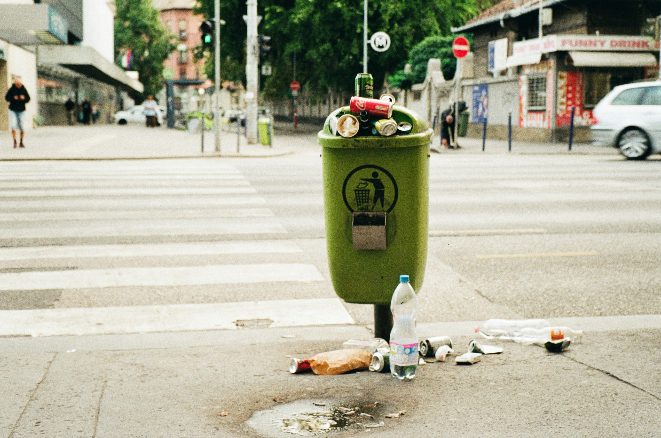 Überquellender grüner Mülleimer an einer Straße mit Müll unter dem Eimer auf dem Gehweg
