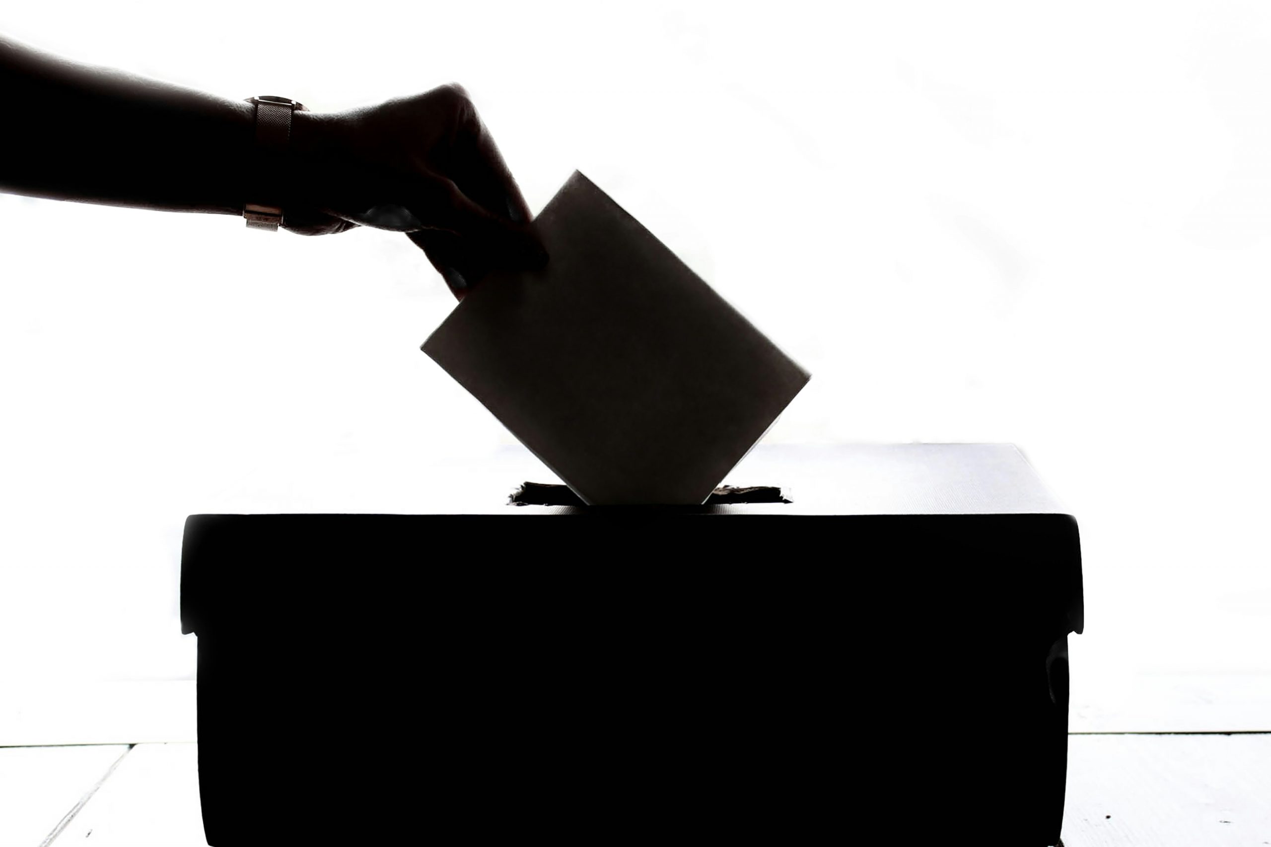 Als Schatten erkennbar, dass ein viereckiges Papier von einer Hand in eine Wahlurne geworfen wird