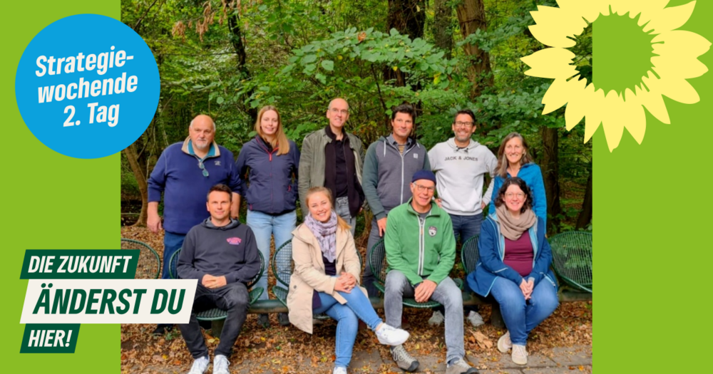 Gruppenbild mit 10 Personen sitzend und stehend vor einem Wald mit der Aufschrift Strategiewochenende 2. Tag, die Zukunft änderst du hier!