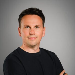 Portraitaufnahme Mario Findeklee vor grauem Hintergrund