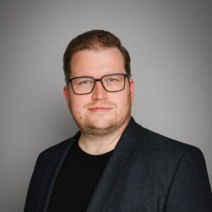 Portraitaufnahme Christian Sass vor grauem Hintergrund