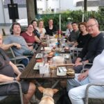 Gruppe an Mitgliedern, die gemeinsam an einem Tisch im Restaurant draußen sitzen und essen und trinken
