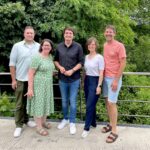 Fünf Mensch stehen auf einer Brücke und lächeln in die Kamera.
